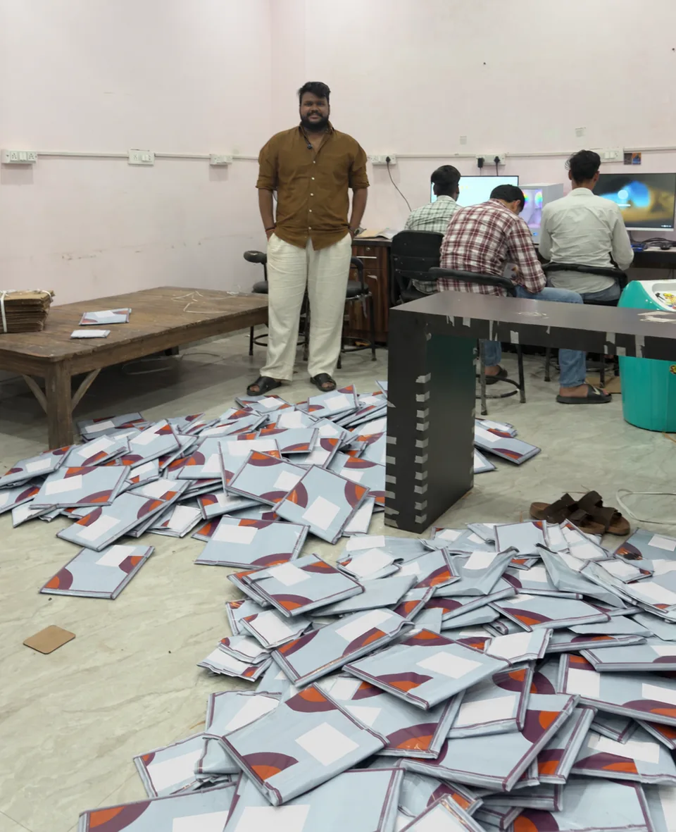 Nikhil Soni standing behind packed parcels, with the team working at computers in the background.